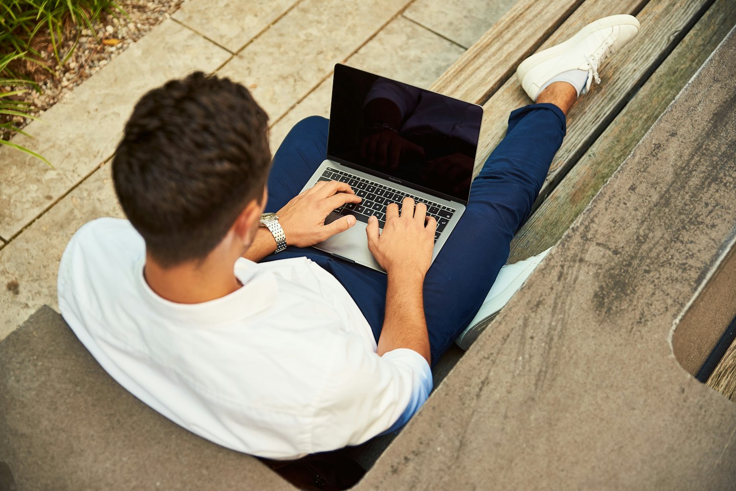 Persona digita su un laptop seduta su una panchina all'aperto.